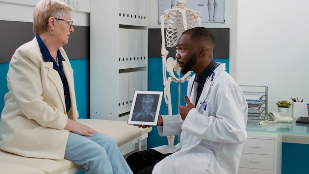 Health specialist analyzing x ray scan on digital tablet with\
senior patient, talking about bones radiography results. doing\
diagnosis examination at medical appointment in healthcare\
clinic.