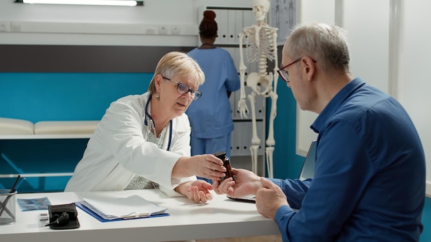 Health specialist consulting senior patient to give bottle of pills as treatment against disease. Prescription medicine in flask with drugs, vitamins and painkillers for sickness recovery.