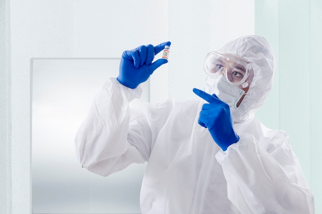 Health worker man with a protective suit and gloves holding covid 19 vaccines on the hospital