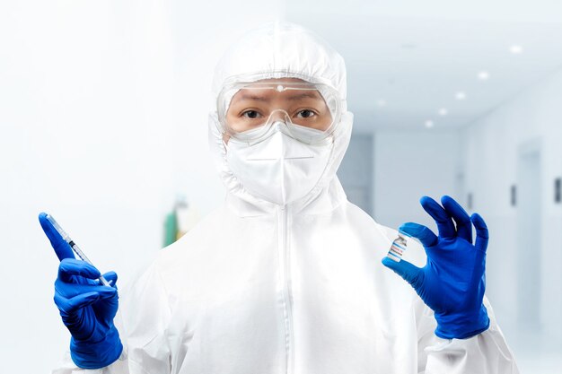 Health worker woman with a protective suit and gloves holding covid 19 vaccines on the hospital