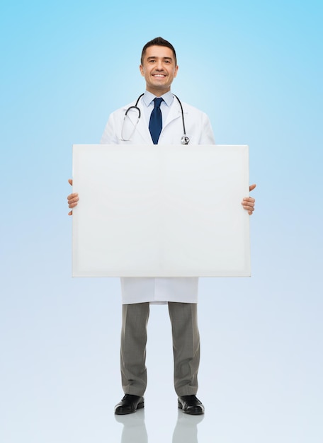 healthcare, advertisement, people and medicine concept - smiling male doctor in white coat holding white blank board over blue background