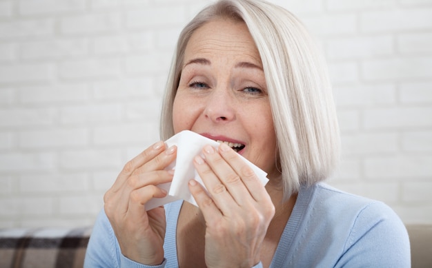 Healthcare, cold, allergy and sick woman blowing her runny nose in paper tissue.