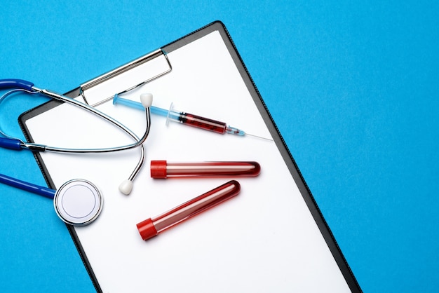 Healthcare concept - stethoscope, blood test tube, syringe and clipboard with blank sheet