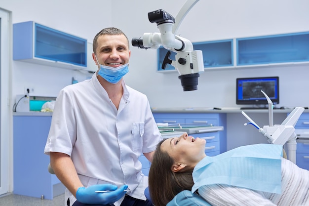 Healthcare dentistry medicine, male doctor dentist treating teeth to a woman patient in chair using dental equipment, tools and microscope, clinic office interior background