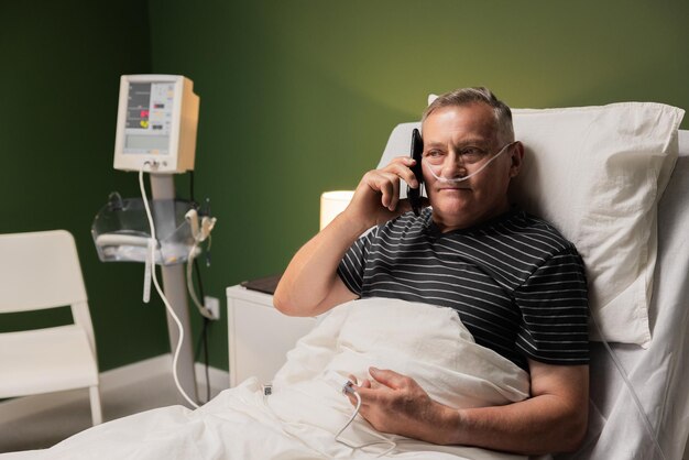 In healthcare facility an older patient lies in bed with an oxygen tube staying in touch through a