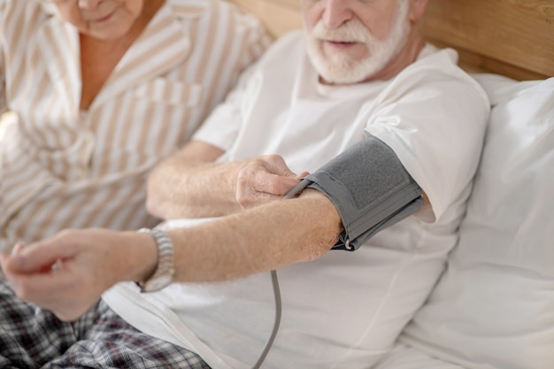 Healthcare. Grey-haired elderly man checking his blood pressure and looking concentrated