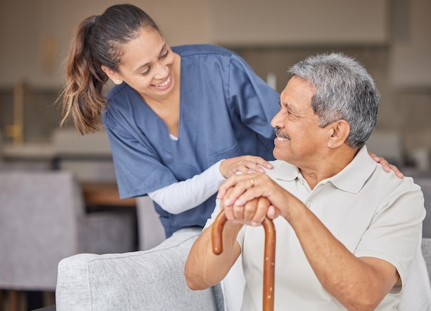 Healthcare kindness and support with nurse helping elderly patient in assisted living home smile and content Happy senior man bonding with a friendly caregiver talking and laugh together on sofa