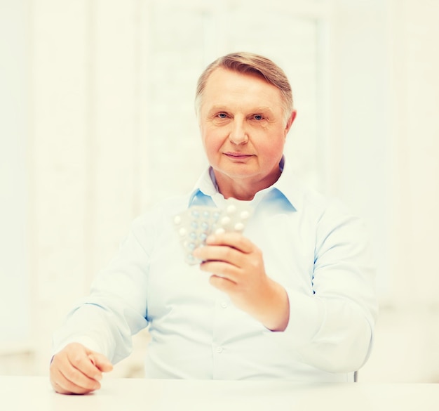 healthcare, madicine, pharmacy and elderly concept - old man with pack of pills