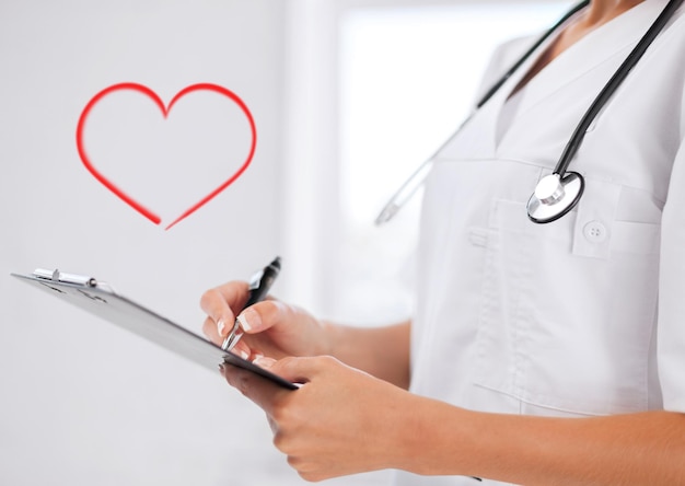 Healthcare and medical concept - female doctor with stethoscope writing prescription