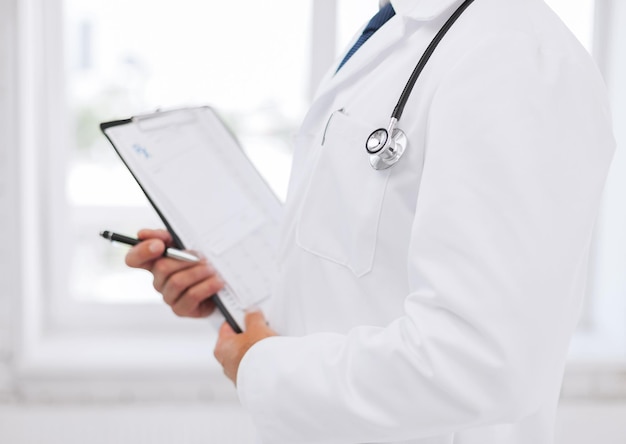 healthcare and medical concept - male doctor with stethoscope writing prescription