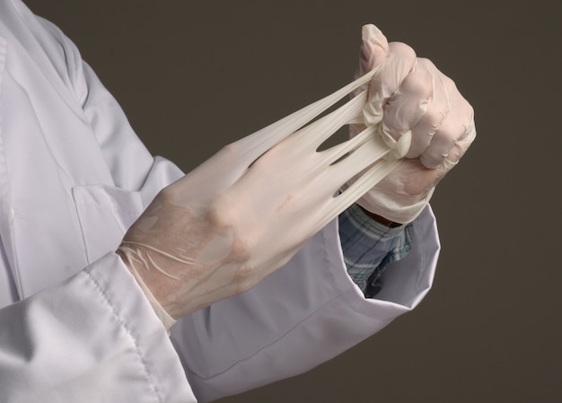 Healthcare and medical concept. Man taking off latex disposable surgical gloves over grey wall