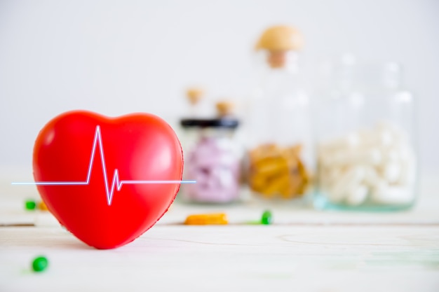 Foto concetto di assistenza sanitaria e medica. cuore rosso sul tavolo di legno con set di bottiglie di medicina e pillole di medicina