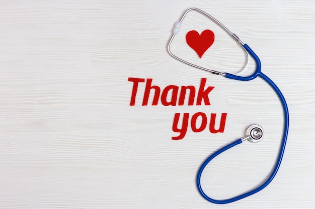 Healthcare and medical concept. Stethoscope blue colored, red heart and text "thank you" on white wooden background with copy space. National Nurses Day.