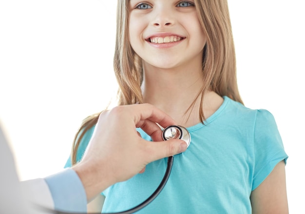 healthcare, medical exam, people, children and medicine concept - close up of happy girl and doctor hand with stethoscope listening to heartbeat