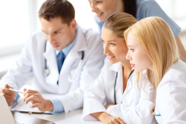 healthcare, medical and technology concept - smiling group of doctors looking at laptop computer in hospital