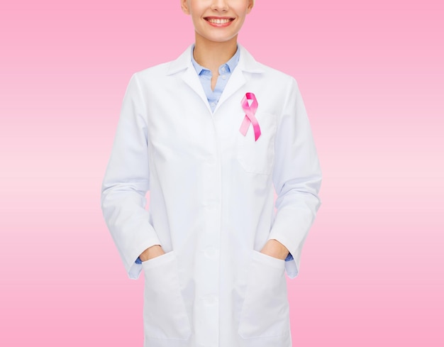 healthcare and medicine concept - close up of smiling female doctor with pink cancer awareness ribbon over pink background