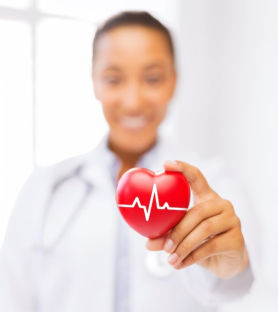 Photo healthcare and medicine concept - female african american doctor holding red heart with ecg line