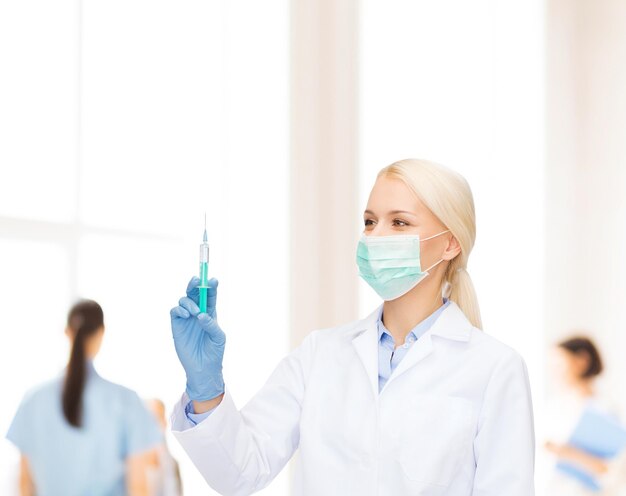 концепция здравоохранения и медицины - женщина-врач в маске и перчатках держит шприц с инъекцией на синем фоне