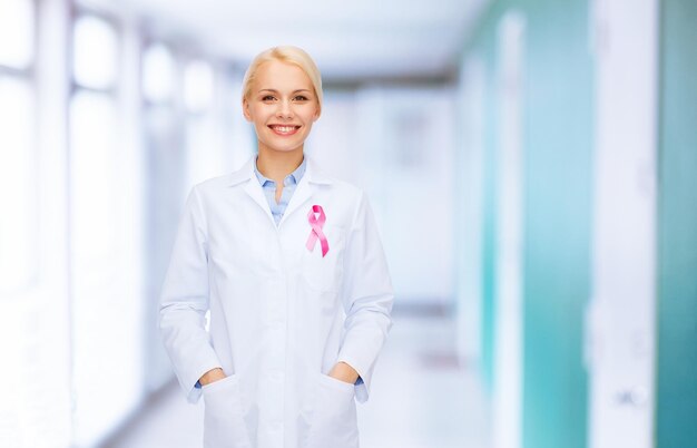 healthcare and medicine concept - smiling female doctor with pink cancer awareness ribbon over hospital background