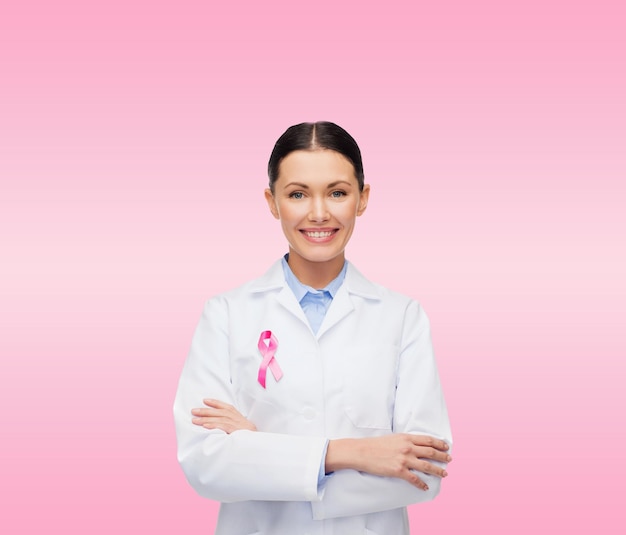 Concetto di assistenza sanitaria e medicina - dottoressa sorridente con nastro rosa per la consapevolezza del cancro su sfondo rosa