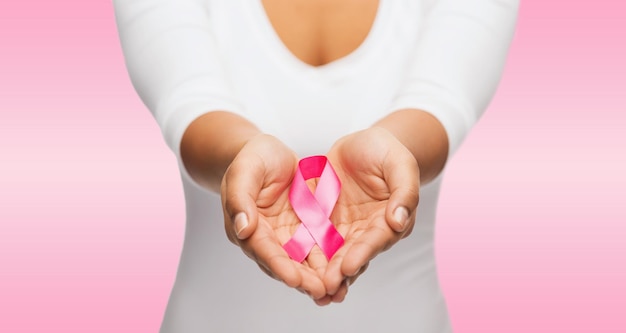 healthcare and medicine concept - womans hands holding pink breast cancer awareness ribbon