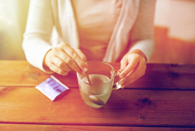 Healthcare, medicine and people concept - close up of woman stirring medication in cup with spoon