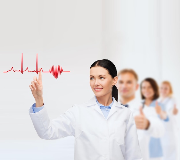 healthcare, medicine and technology concept - smiling female doctor pointing to heart and cardiogram