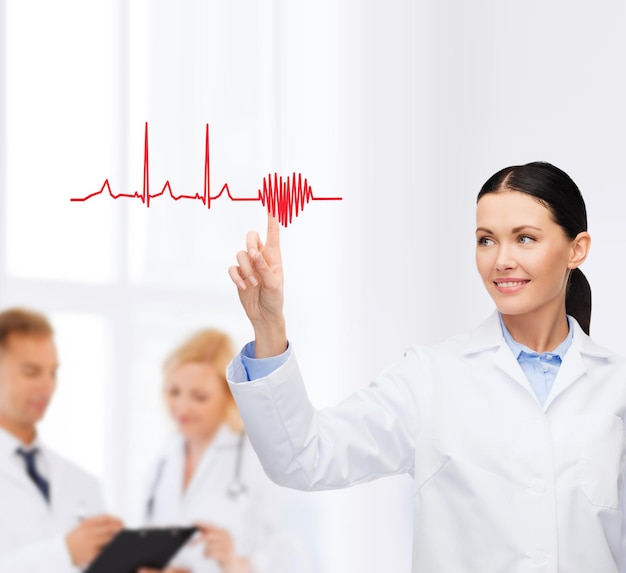 Foto concetto di assistenza sanitaria, medicina e tecnologia - dottoressa sorridente che punta al cuore e al cardiogramma