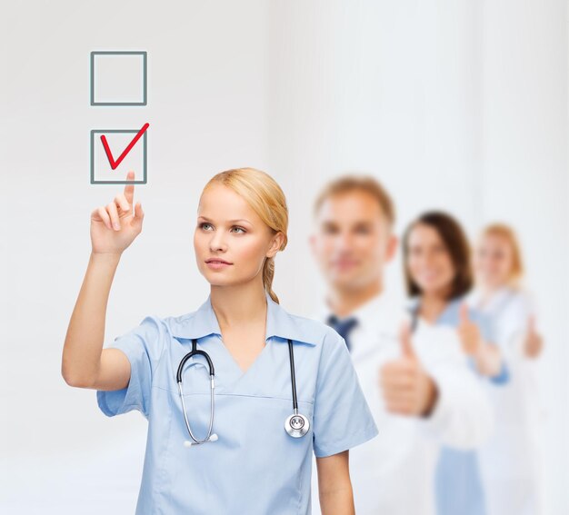 ヘルスケア、医学、技術の概念-チェックボックスの赤いチェックマークを指している若い医師や看護師の笑顔