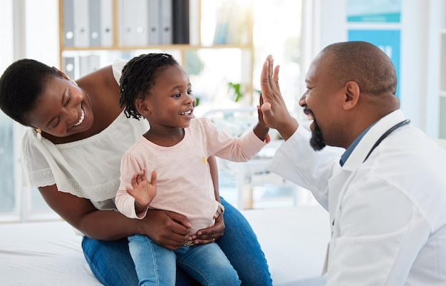 Healthcare mother and girl gives doctor high five in a doctors office Medical insurance healthy child development and consulting in a doctors office Black woman daughter and pediatrician smiling