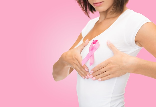 healthcare, people, charity and medicine concept - close up of woman in t-shirt with breast cancer awareness ribbon over pink background