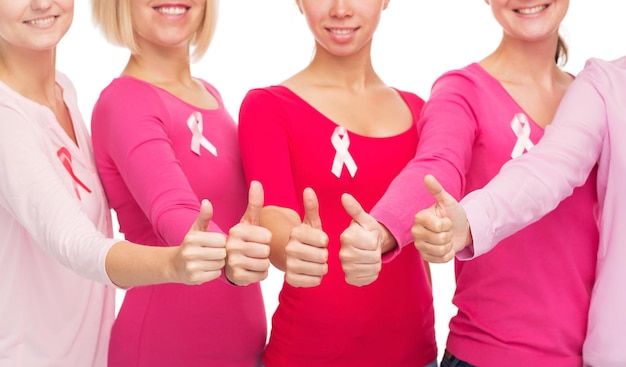 Foto concetto di assistenza sanitaria, persone, gesto e medicina - primo piano di donne sorridenti in camicie bianche con nastri rosa per la consapevolezza del cancro al seno che mostrano i pollici in su su sfondo bianco