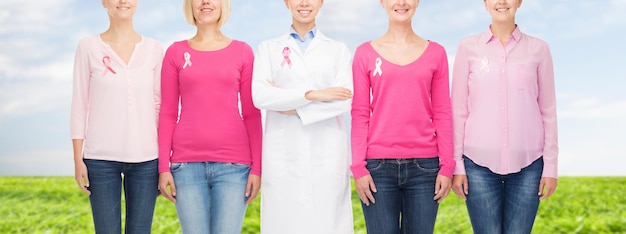 의료, 사람, 의학 개념 - 푸른 하늘과 잔디 배경 위에 분홍색 유방암 인식 리본이 달린 빈 셔츠를 입은 웃고 있는 여성들의 클로즈업