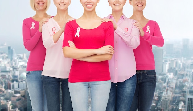 Foto concetto di assistenza sanitaria, persone e medicina - primo piano di donne sorridenti in camicie bianche con nastri rosa per la consapevolezza del cancro al seno sullo sfondo della città