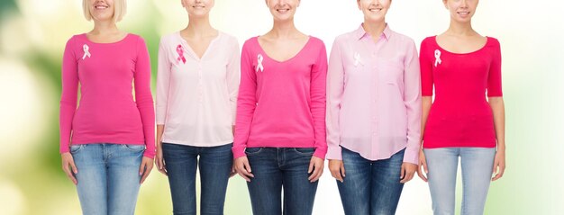 healthcare, people and medicine concept - close up of smiling women in blank shirts with pink breast cancer awareness ribbons over green background