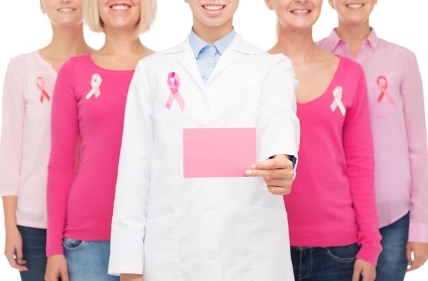 ヘルスケア、人と医学の概念-ピンクの乳がん啓発リボンと白い背景の上の白紙のカードとシャツを着た笑顔の女性のクローズアップ
