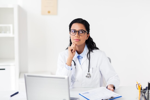 healthcare, people and medicine concept - female doctor in white coat with laptop computer and clipboard at hospital