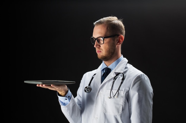 ヘルスケア、人、技術、医学のコンセプト – 黒い背景に聴診器とタブレット PC コンピューターを持つ白衣を着た男性医師