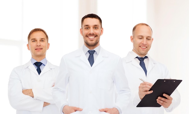 ヘルスケア、職業、医学の概念-クリニックの背景の上にクリップボードと聴診器で白衣を着た笑顔の男性医師のグループ