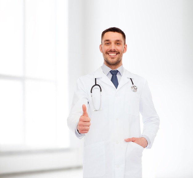 ヘルスケア、職業、医学の概念-白い背景の上に親指を示す聴診器で笑顔の男性医師