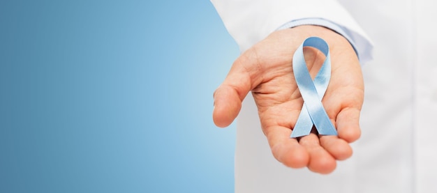 healthcare, profession, people and medicine concept - close up of male doctor hand holding sky blue prostate cancer awareness ribbon over blue background