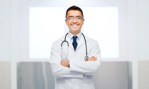 ヘルスケア、職業、人、医学のコンセプト – 白衣を着た笑顔の男性医師と聴診器で眼鏡