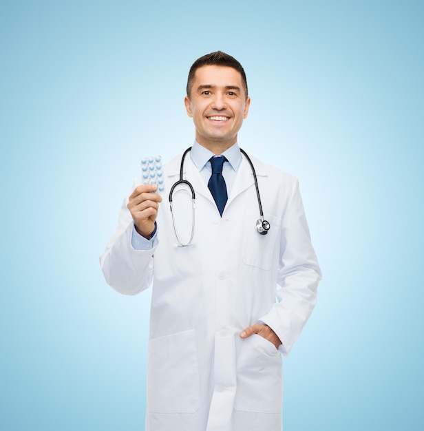 healthcare, profession, people and medicine concept - smiling male doctor in white coat with tablets over blue background