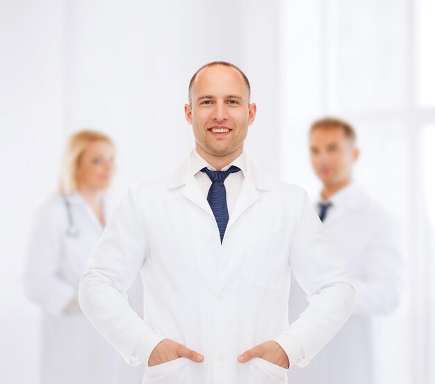 healthcare, profession, teamwork and medicine concept - smiling male doctor in white coat over group of medics