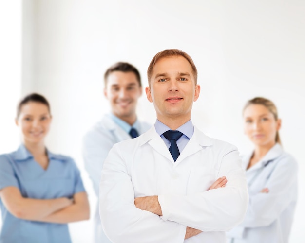 healthcare, profession, teamwork and medicine concept - smiling male doctor in white coat over group of medics