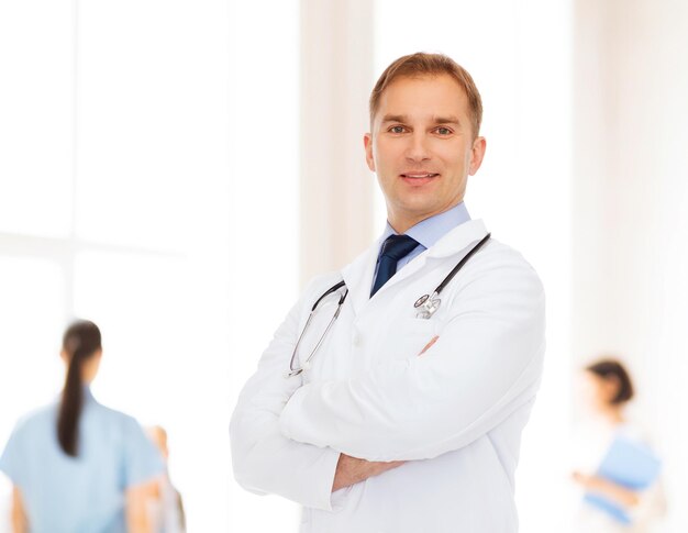 healthcare, profession, teamwork, people and medicine concept - smiling male doctor with stethoscope in white coat over over group of medics