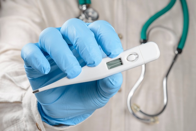 Healthcare professional holding thermometer wearing protective gloves