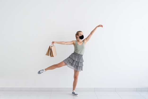 Healthcare and quarantine concept. Young woman dancing ballet with shopping bags in a protective mask.