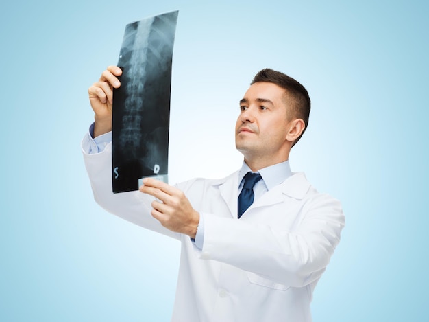 healthcare, roentgen, people and medicine concept - male doctor in white coat looking at x-ray over blue background