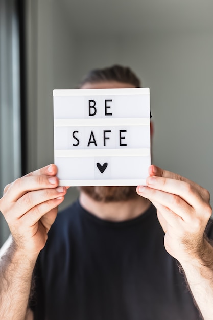 Concetto di assistenza sanitaria e sicurezza. uomo non riconosciuto che tiene un lightbox con testo stai al sicuro durante le pandemie del coronavirus covid-19